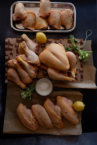 Raw chicken pieces on a cutting board with lemons and herbs on a dark surface