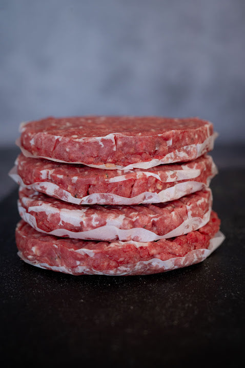 A stack of raw beef burgers, on a dark background.