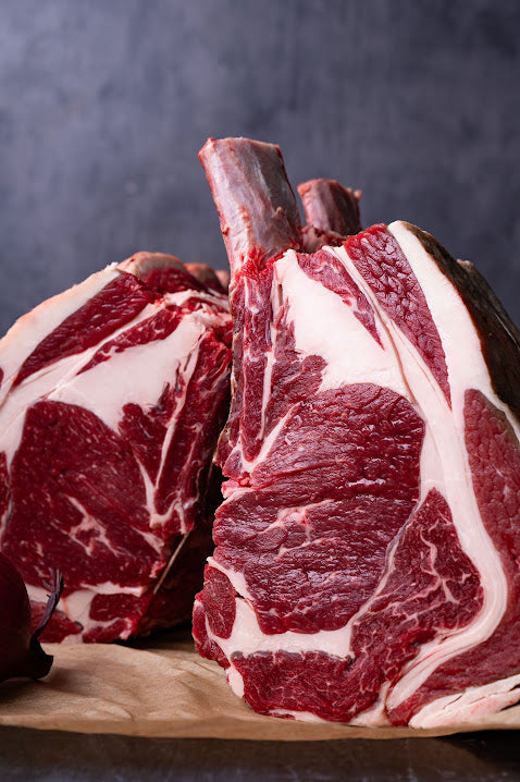 Two raw rib of beef cuts on a wooden board, showing marbled red meat with fat in contrast to the surrounding areas.