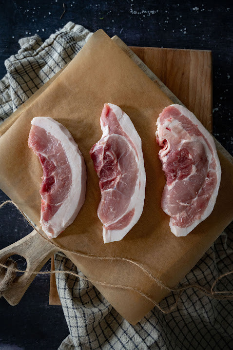 Three raw Berkshire Leg Steaks on a butcher block with a piece of kitchen towel in the background.