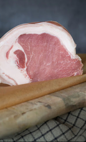 A fresh pork loin joint on a wooden board, with a rind of fat and scoring for crispy crackling.