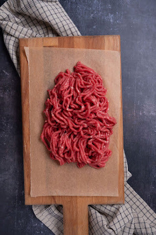 A mound of fresh beef mince on a wooden board, with a checkered napkin in the background.