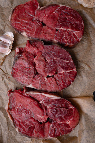 Several pieces of shin beef are laid out on a paper surface, with a piece of garlic near the top.