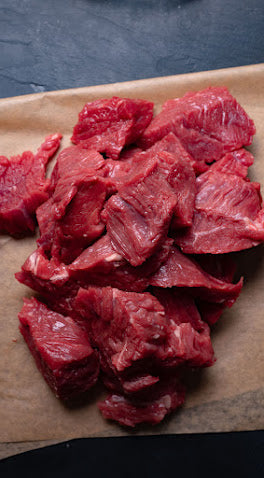 Raw beef chunks on a wooden cutting board