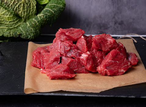 Diced raw beef on a butchers block with a head of cabbage in the background.