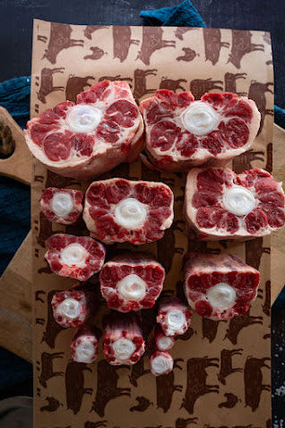 Several pieces of oxtail meat arranged on a cutting board with a brown paper background featuring cow patterns.