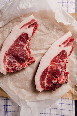 Two raw Mangalitza pork chops on a paper, ready for cooking.
