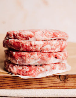 Stack of uncooked pork and apple burgers on a wooden board, wrapped in paper.