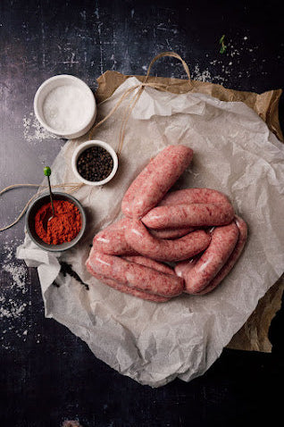 Raw black pepper sausages on a paper, with spices and seasonings around, on a dark textured background.