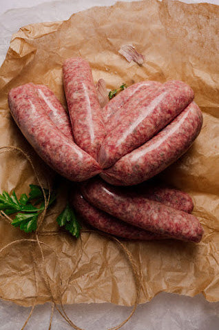 Raw Cumberland sausages on a piece of brown paper, tied with string, garnished with a sprig of parsley.