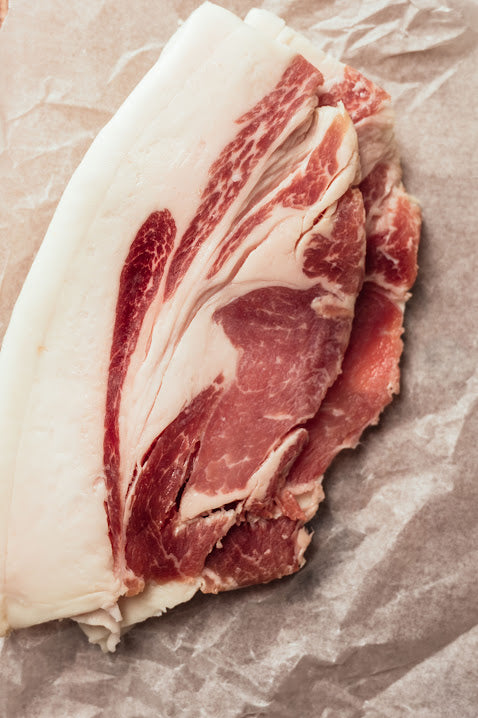 A slice of mangalitza back bacon with a white fat layer and pinkish-red meat, placed on a brown paper surface.