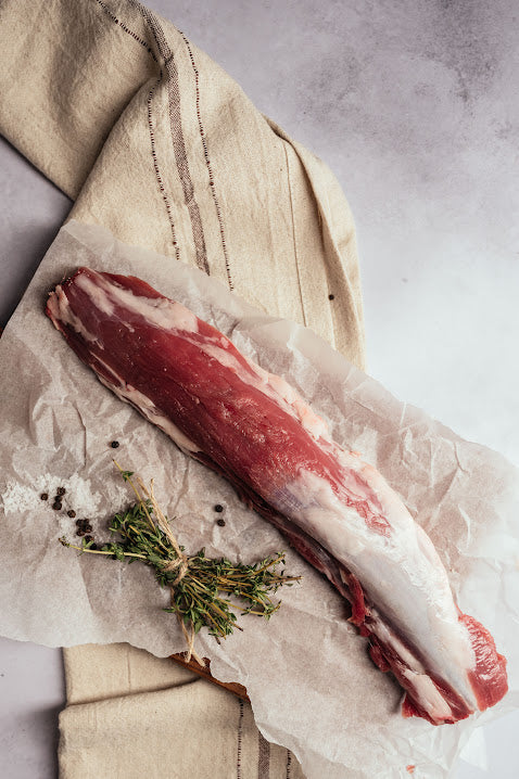 A fresh Mangalitza pork tenderloin on butchers paper, garnished with herbs.