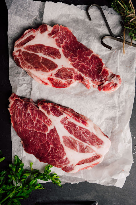 raw pork steaks on butchers paper with sprigs of herbs
