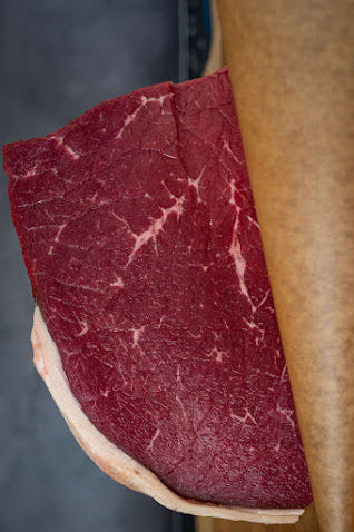 Sliced piece of red meat on a wooden board with a dark background
