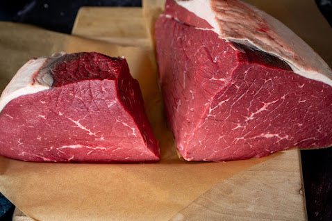 Two pieces of raw beef on a wooden cutting board