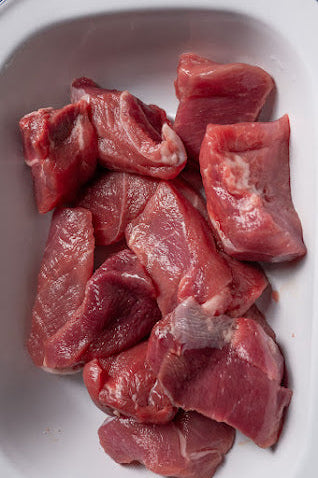 A bowl containing raw diced lamb pieces.