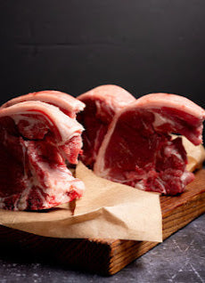 Raw lamb chops on butchers paper and a wooden board, seasoned and ready for cooking.