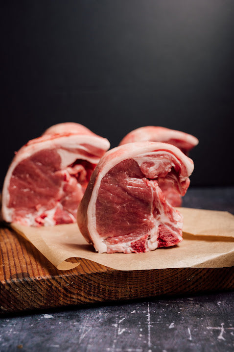 Raw pork chops on butchers paper and a wooden cutting board with a dark background