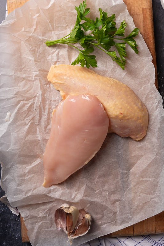 Fresh free range chicken breast on paper and chopping board with herbs and garlic