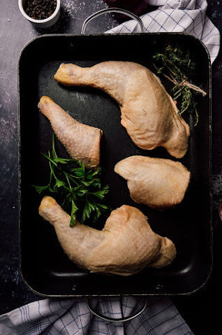 Raw chicken legs on a black tray with herbs on a dark surface